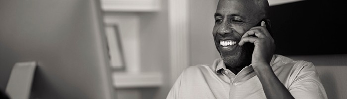 A smiling Black man in a collared shirt holds his phone to his ear.